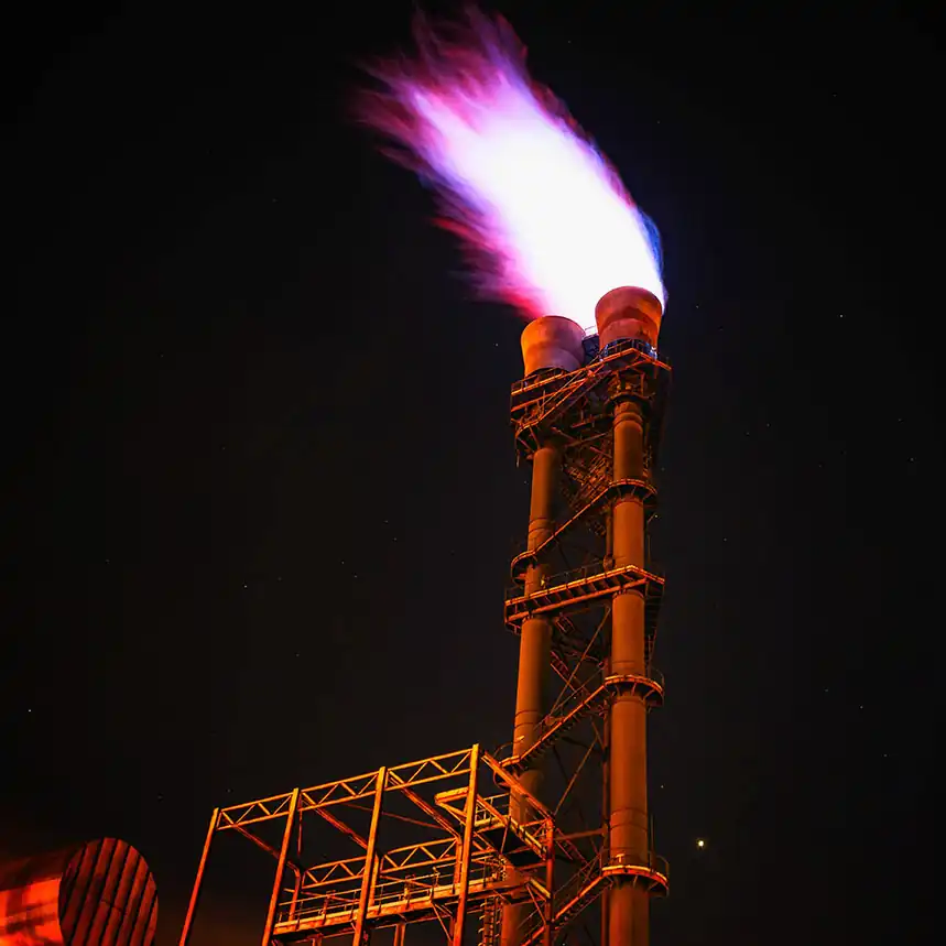 Cheminée d'usine à gaz surmontée d'une flamme sur fond de ciel nocturne